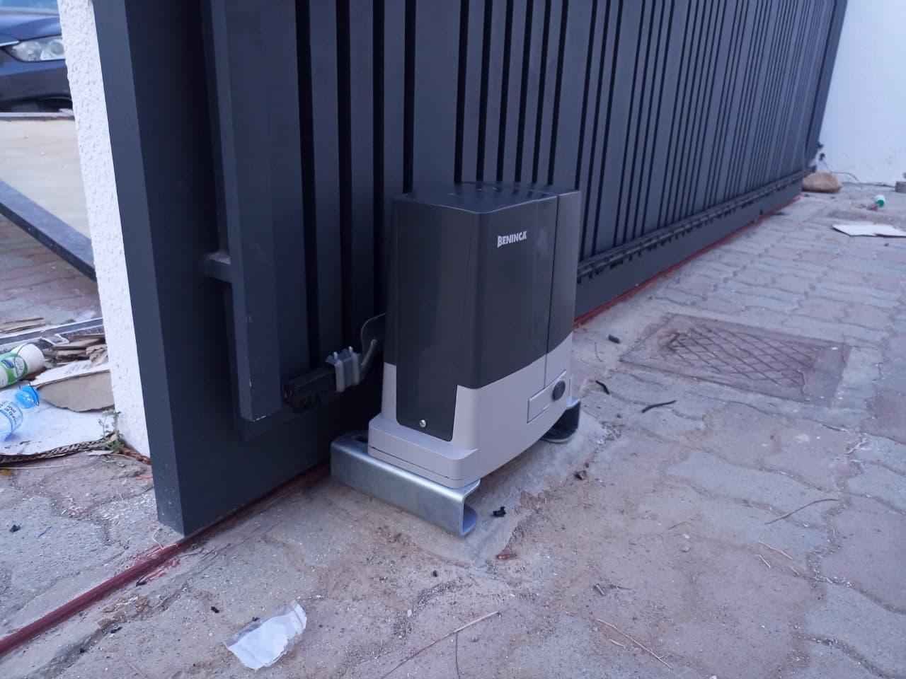 Beninca sliding gate motor mounted on a galvanised base plate beside a dark slatted sliding gate in Oman