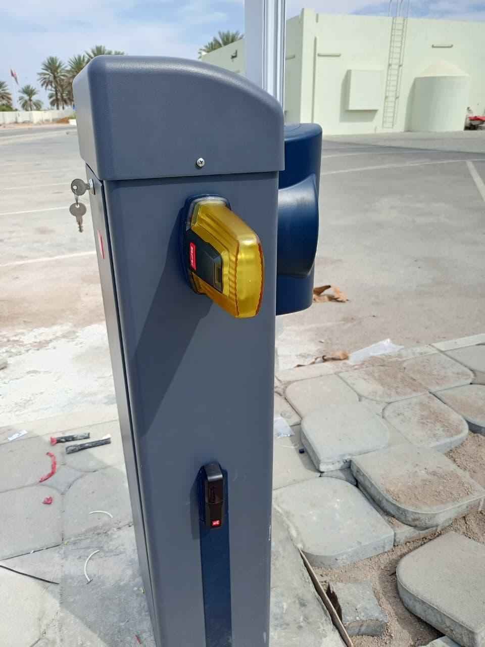 Close view of a BFT boom barrier showing the amber warning beacon and the safety photocell