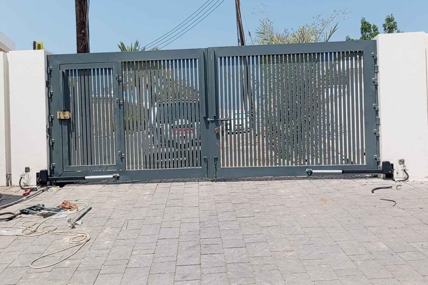 Two linear swing gate operators fitted to a modern grey double gate with a pedestrian door at a villa in Oman
