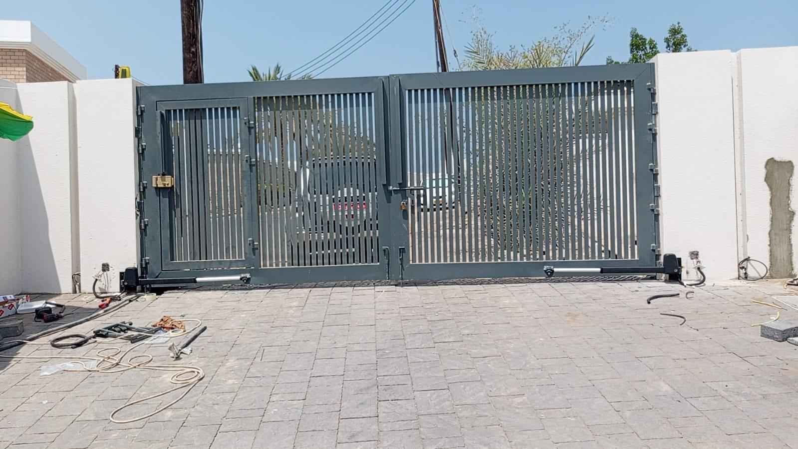 Two linear swing gate operators fitted to a modern grey double gate with a pedestrian door in Oman