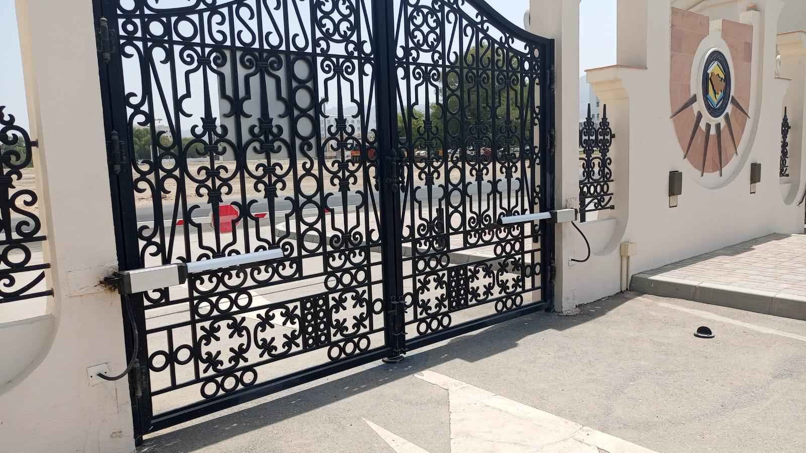 Linear swing gate operators fitted to an ornate iron gate at an institutional entrance in Oman